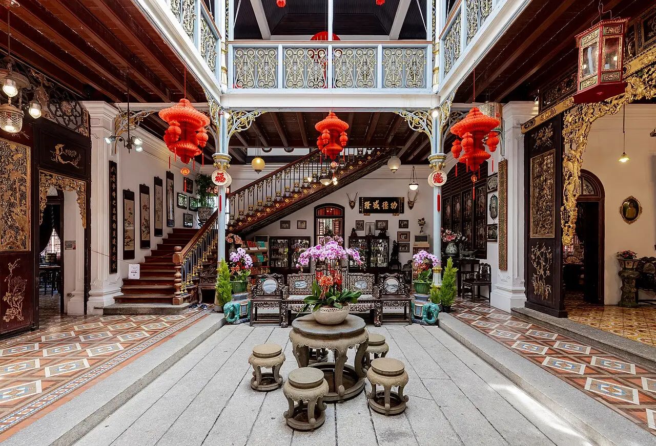 Opulent interior of Pinang Peranakan Mansion, showcasing a grand courtyard, intricate carvings, traditional furniture, and red lanterns
